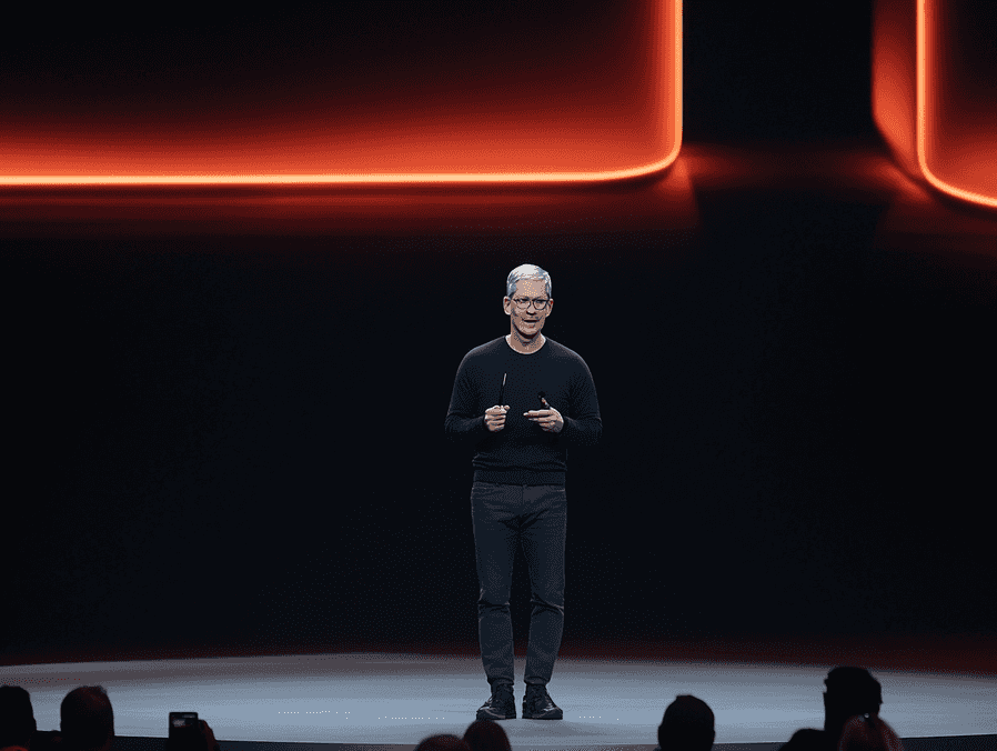 Tim Cook speaking at a tech conference, addressing a large audience